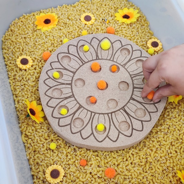 Enfant plaçant des pompons colorés dans un plateau de motricité fine en forme de tournesol en bois MDF