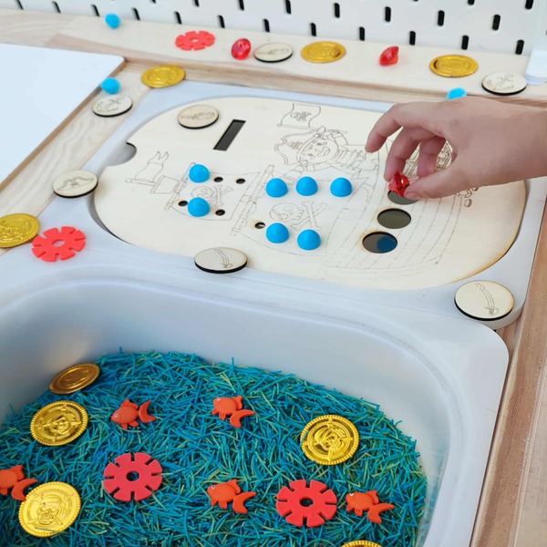 Enfant jouant avec un insert pirate en bois, jetons colorés et trésors pour motricité fine