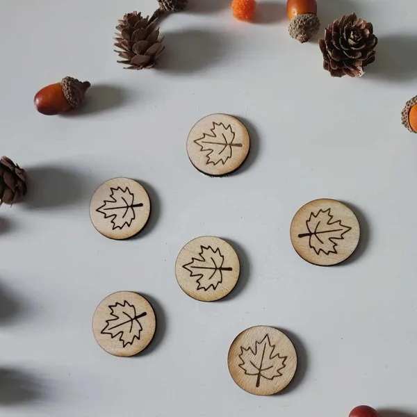 Jetons en bois gravés de feuilles d’érable disposés pour une activité sensorielle inspirée de l’automne