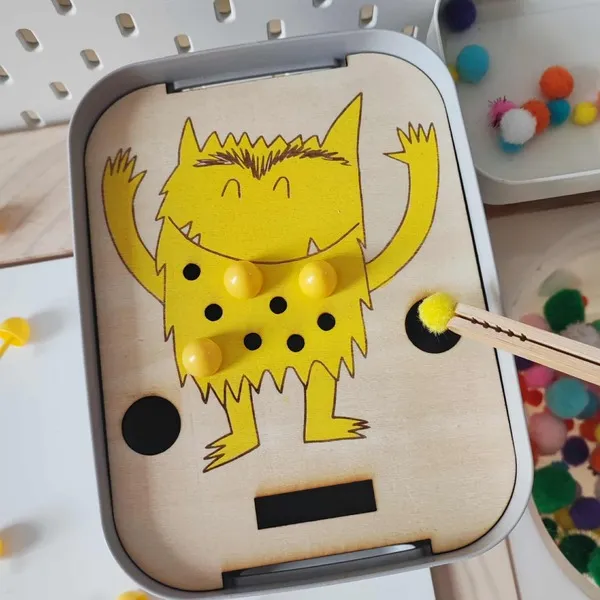 Activité sensorielle avec monstre de la joie jaune et pompons sur support en bois