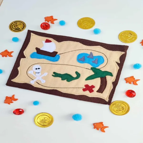 Carte pirate en feutrine artisanale entourée de pièces d’or et accessoires sensoriels