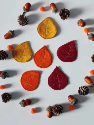 Feuilles en feutrine colorées entourées de pommes de pin, glands et pompons pour activité sensorielle d’automne
