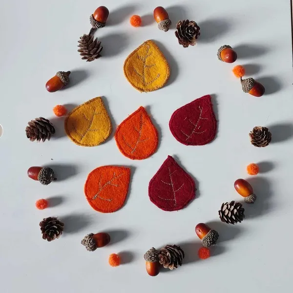 Feuilles en feutrine colorées entourées de pommes de pin, glands et pompons pour activité sensorielle d’automne