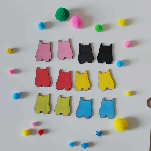 Petits jetons en bois colorés en forme de monstres disposés en rangées avec des pompons sensoriels autour