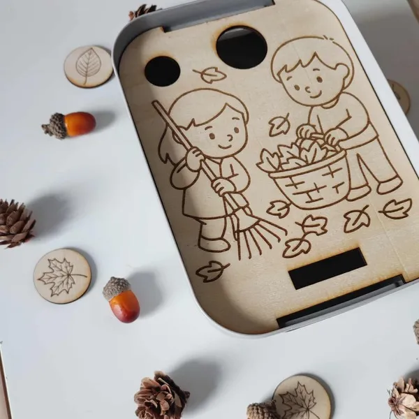 Détail d’un plateau sensoriel en bois illustrant deux enfants ramassant des feuilles d’automne – activité Montessori