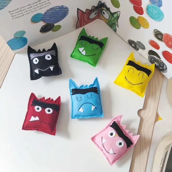 Six petits monstres en feutrine colorée représentant différentes émotions disposés sur une table d’activité Montessori