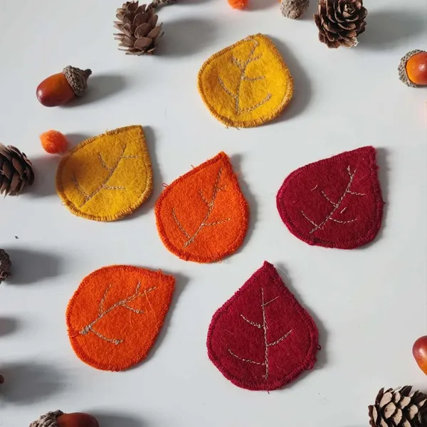 Feuilles d’automne en feutrine faites main dans des tons rouges, oranges et jaunes, entourées d’éléments naturels