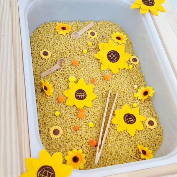 Bac sensoriel rempli de pâtes avec fleurs en feutrine tournesol, pompons et petits outils en bois Montessori