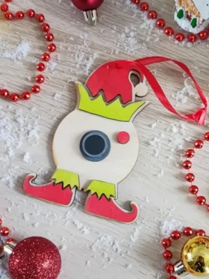 Décoration artisanale en bois en forme de lutin de Noël avec bonnet rouge et bottes colorées entourée de fausse neige et boules festives