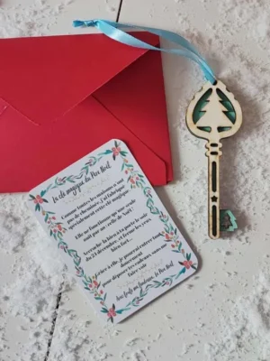 Clé magique du Père Noël en bois sapin bleu avec ruban, carte explicative et enveloppe rouge sur fond enneigé de décor de fête