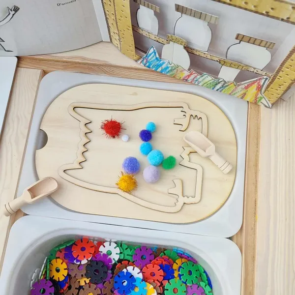 Activité sensorielle inspirée du Monstre des émotions avec insert en bois et pompons colorés dans une table d’exploration