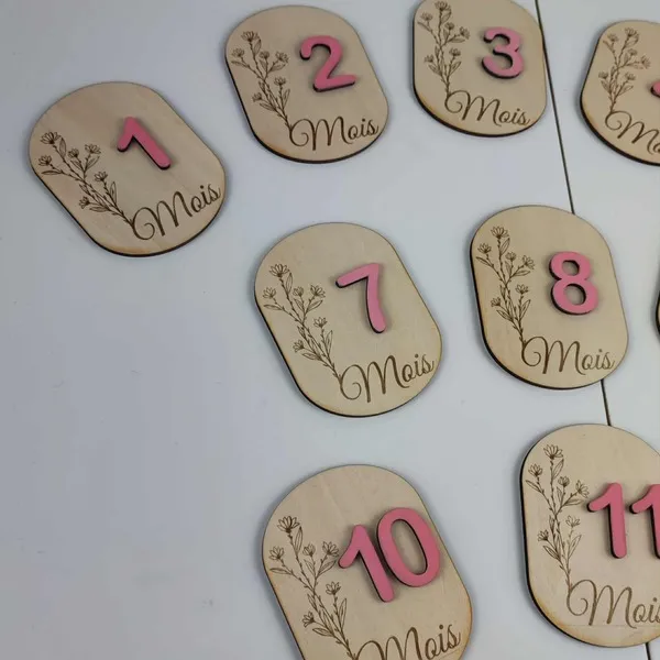 Zoom sur des cartes étapes en bois gravées de fleurs et numérotées en rose pour suivre les mois de bébé