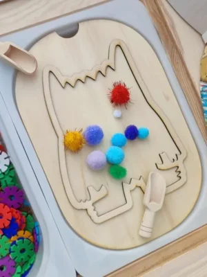 Insert en bois du Monstre des émotions utilisé pour une activité sensorielle avec pompons colorés et cuillères de motricité fine