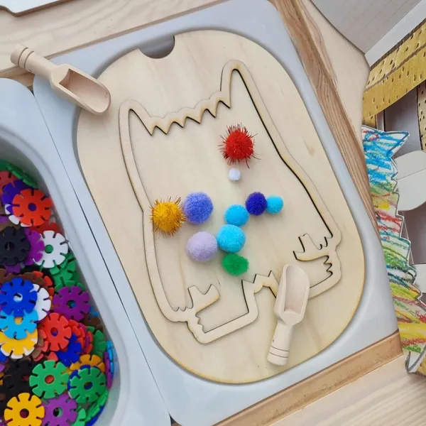 Insert en bois du Monstre des émotions utilisé pour une activité sensorielle avec pompons colorés et cuillères de motricité fine