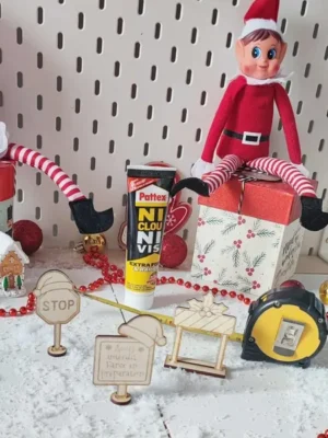 Mise en scène de lutins farceurs bricolant avec colle, mètre ruban et panneaux en bois sur fond de Noël enneigé