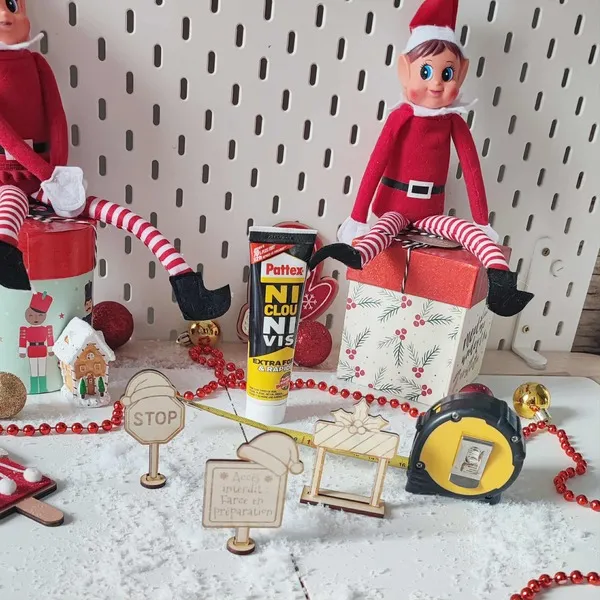 Mise en scène de lutins farceurs bricolant avec colle, mètre ruban et panneaux en bois sur fond de Noël enneigé