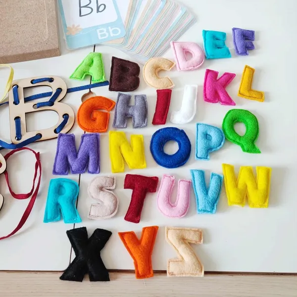Lettres de l’alphabet en feutrine multicolore disposées sur une table d’apprentissage Montessori avec cartes de lecture et lettres à lacer en bois