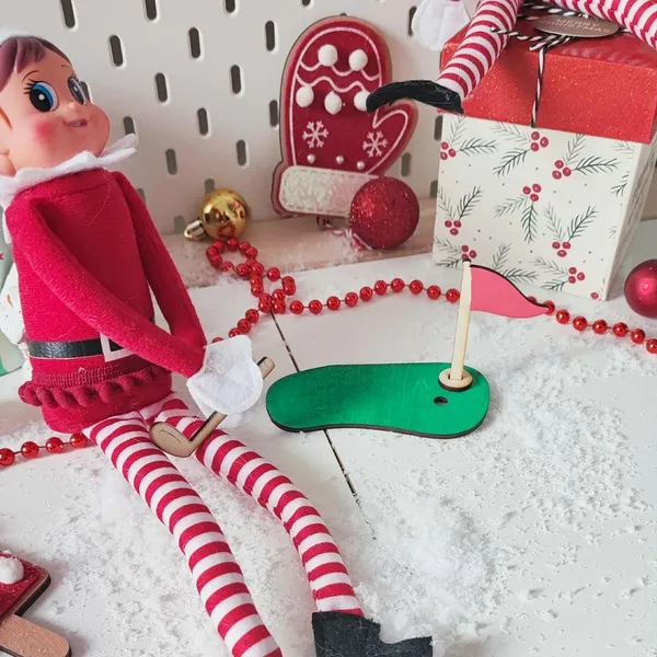 Lutin farceur jouant au mini-golf avec accessoires en bois, drapeau rouge et décor de Noël enneigé