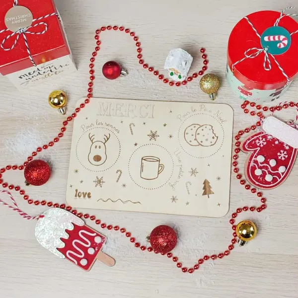 Plateau en bois gravé pour déposer les biscuits du Père Noël et la carotte des rennes, entouré de décorations festives rouges et dorées