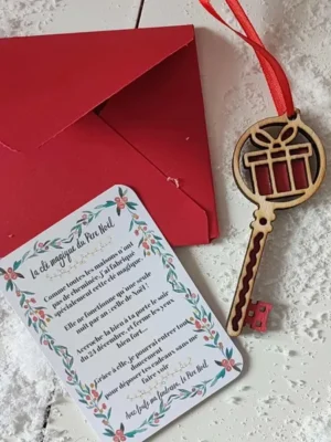 Clé magique du Père Noël en bois motif cadeau rouge avec ruban, carte explicative et enveloppe rouge posées sur un fond enneigé