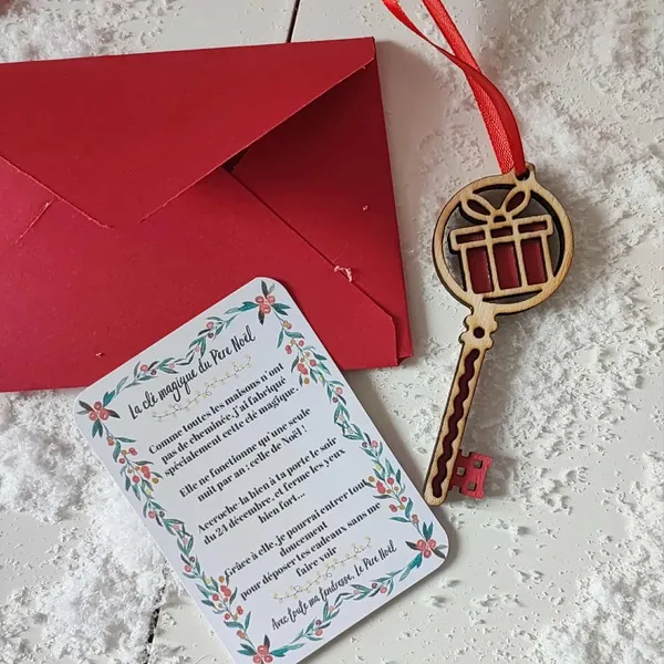 Clé magique du Père Noël en bois motif cadeau rouge avec ruban, carte explicative et enveloppe rouge posées sur un fond enneigé
