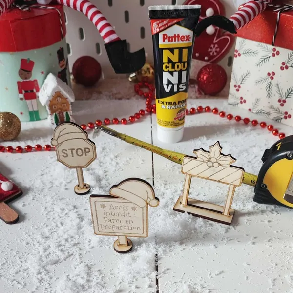 Panneaux en bois gravés “Accès interdit : farce en préparation” et “STOP” installés dans un décor de Noël avec outils et neige artificielle