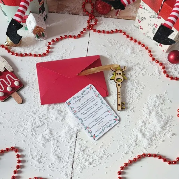 Clé magique du Père Noël en bois avec ruban doré, carte explicative et enveloppe rouge sur fond enneigé décoré d’éléments festifs de Noël