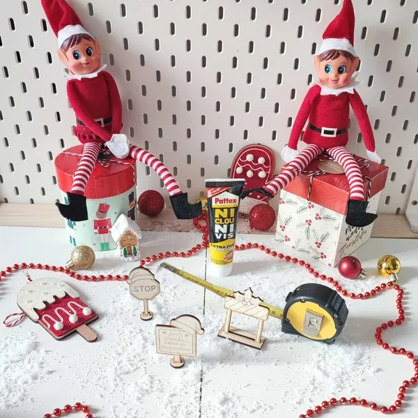 Scène de lutins farceurs de Noël avec outils, colle, panneaux en bois gravé et décor enneigé festif