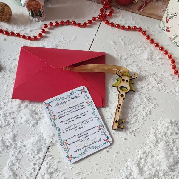Clé magique du Père Noël en bois avec ruban doré, carte illustrée et enveloppe rouge sur fond enneigé et décorations de Noël