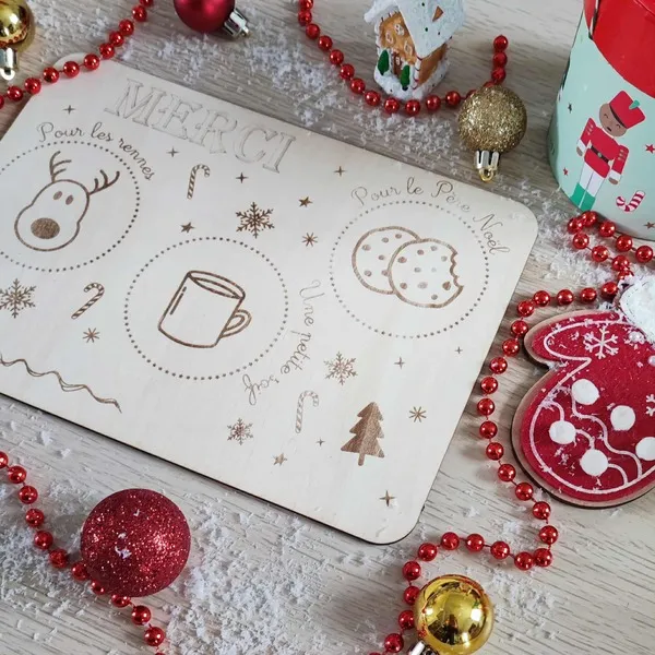 Plateau en bois gravé pour le Père Noël et ses rennes, entouré de décorations rouges, dorées et neige artificielle