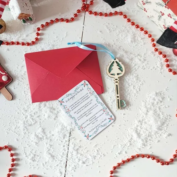 Clé magique du Père Noël en bois sapin bleu avec carte et enveloppe rouge sur fond enneigé décoré de guirlandes rouges et d’éléments de Noël