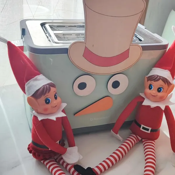 Deux lutins farceurs de Noël assis devant un grille-pain décoré en bonhomme de neige avec chapeau, yeux et nez en bois