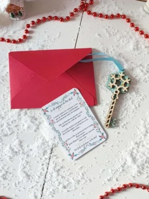 Clé magique du Père Noël en bois flocon bleu avec ruban, carte explicative et enveloppe rouge sur fond enneigé décoré d’éléments de Noël