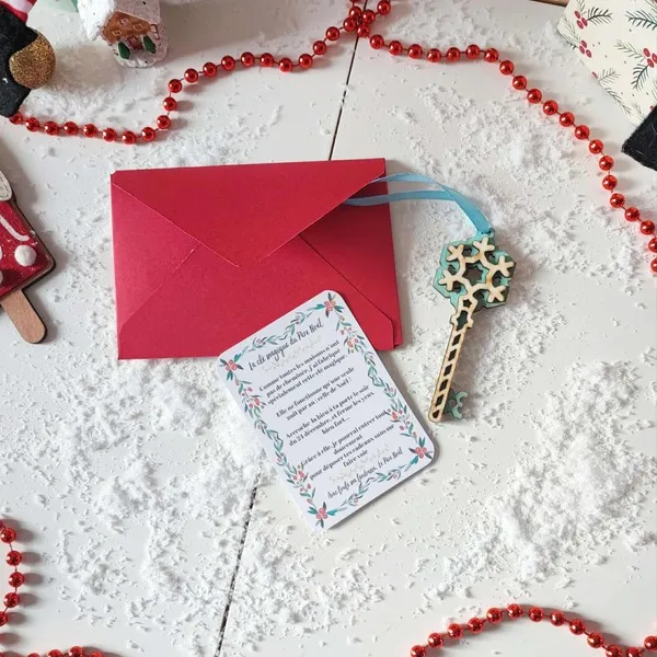 Clé magique du Père Noël en bois flocon bleu avec ruban, carte explicative et enveloppe rouge sur fond enneigé décoré d’éléments de Noël