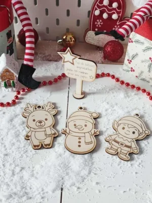 Décor de Noël enneigé avec trois ornements en bois gravé – renne, bonhomme de neige, lutin – et un panneau étoilé “Pas de bêtises aujourd’hui, juste un cadeau pour ton sapin”