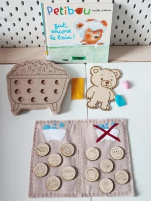 Activité éducative inspirée du livre “Petibou zut encore le bain !” avec ours en bois, baignoire à picots et jetons gravés sur le thème de l’hygiène et du quotidien
