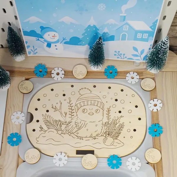 Plateau sensoriel en bois gravé d’un petit oiseau hivernal avec bonnet, décoré de jetons flocons et de sapins miniatures pour activité Montessori d’hiver