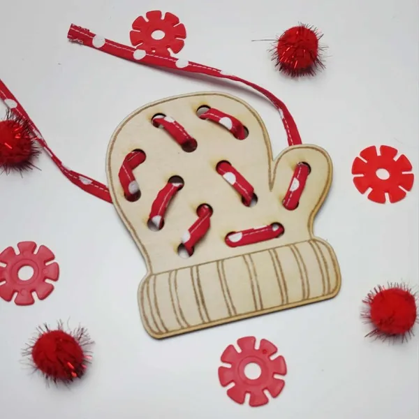 Carte à lacer en bois en forme de moufle, lacée avec un ruban rouge à pois blancs et entourée d’éléments sensoriels rouges.