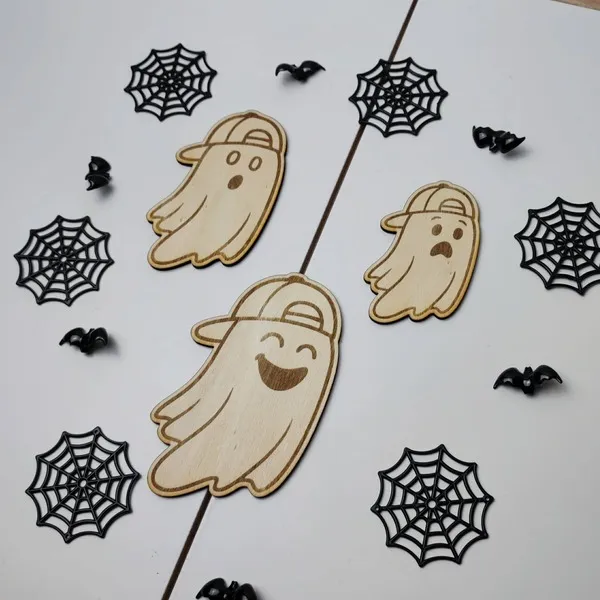 Trois fantômes en bois de tailles différentes, chacun avec une expression unique et une casquette, entourés de toiles d’araignée noires et de petites chauves-souris décoratives.
