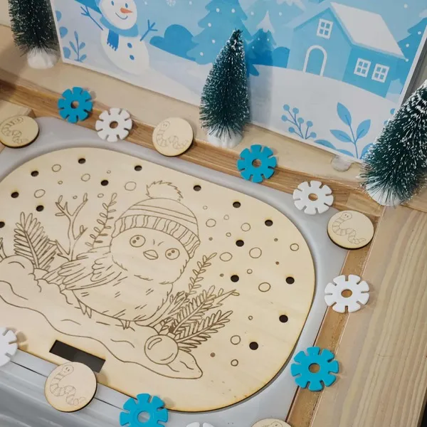 Plateau Montessori en bois gravé d’un oiseau d’hiver avec bonnet, entouré de sapins miniatures et de jetons flocons bleus et blancs
