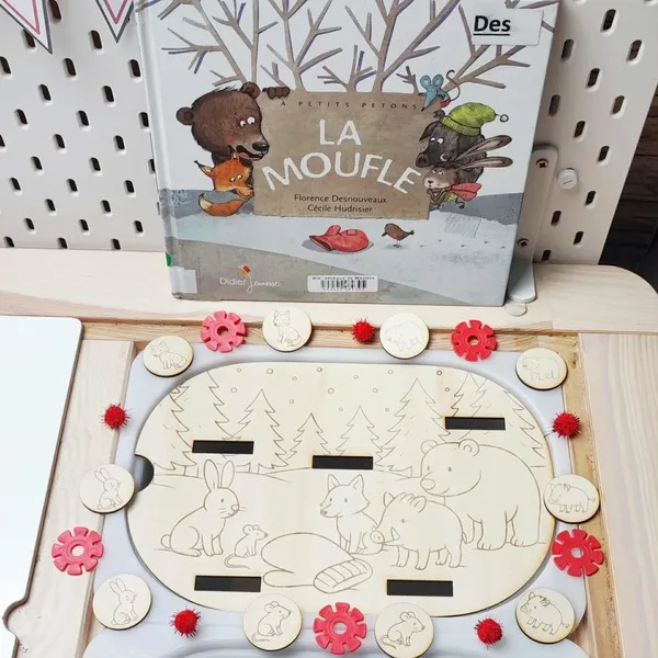 Plateau en bois thème La Moufle avec animaux gravés et jetons assortis, présenté devant le livre d’histoire