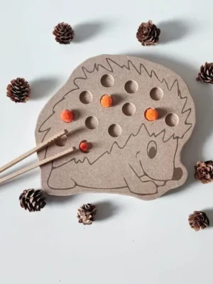 Plateau de motricité fine en forme de hérisson avec pompons orange, décoré de petites pommes de pin.