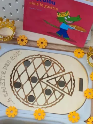 Plateau en bois gravé représentant une galette des rois avec jetons noirs, couronnes dorées et livre Crocolou aime la galette