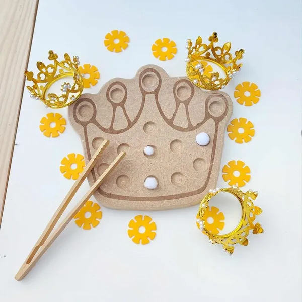Plateau de motricité fine en bois en forme de couronne, accompagné de pinces, de pompons blancs et de petites couronnes dorées pour une activité sur le thème de la galette des rois