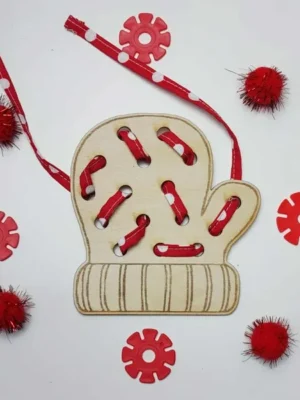 Carte à lacer en forme de moufle en bois, lacée avec un ruban rouge à pois et entourée d’éléments rouges décoratifs.