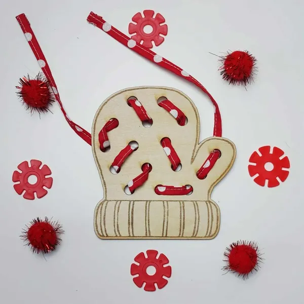Carte à lacer en forme de moufle en bois, lacée avec un ruban rouge à pois et entourée d’éléments rouges décoratifs.