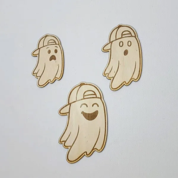Trois fantômes en bois aux expressions différentes, chacun gravé avec une casquette, disposés sur un fond blanc.