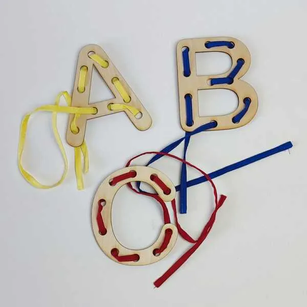 Lettres en bois A, B et C à lacer entourées de pièces colorées dispersées.