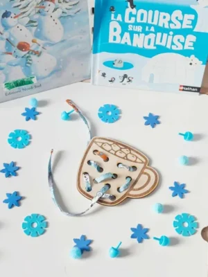 Carte à lacets en bois en forme de tasse de chocolat chaud, décorée sur le thème de l’hiver avec accessoires bleus et livres sur la banquise en arrière-plan