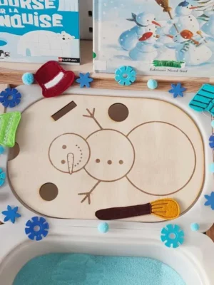 Insert en bois bonhomme de neige décoré d’accessoires en feutrine et éléments sensoriels bleus sur plateau d’activité banquise